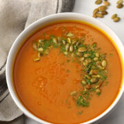 A bowl of pumpkin carrot soup topped with pumpkin seeds and parsley.