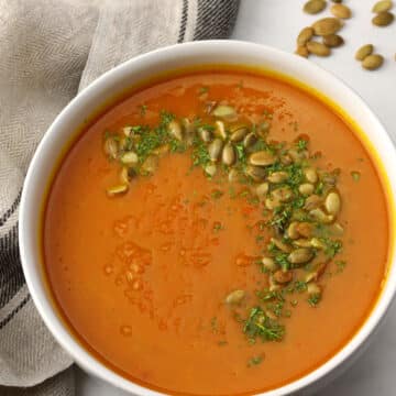 A bowl of pumpkin carrot soup topped with pumpkin seeds and parsley.