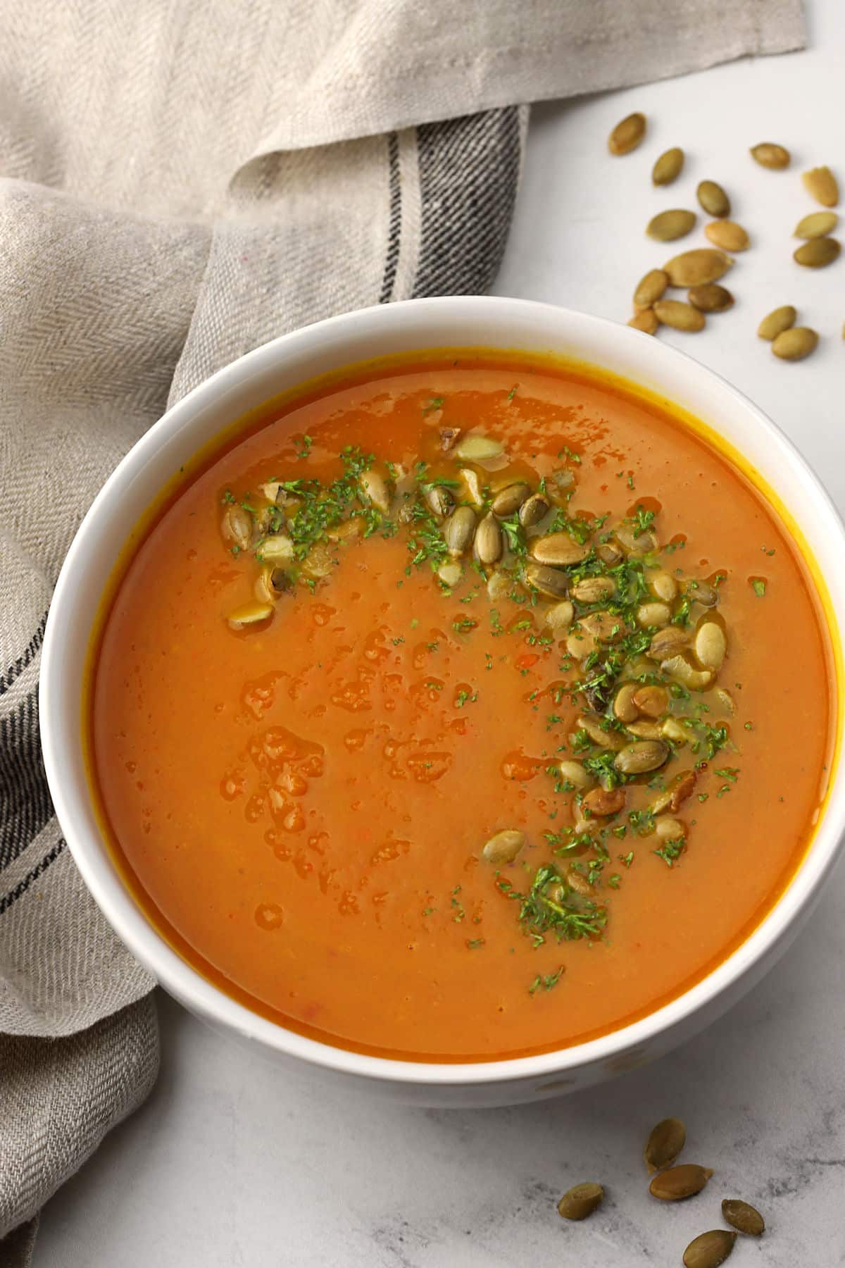 A bowl of pumpkin carrot soup topped with pumpkin seeds and parsley.