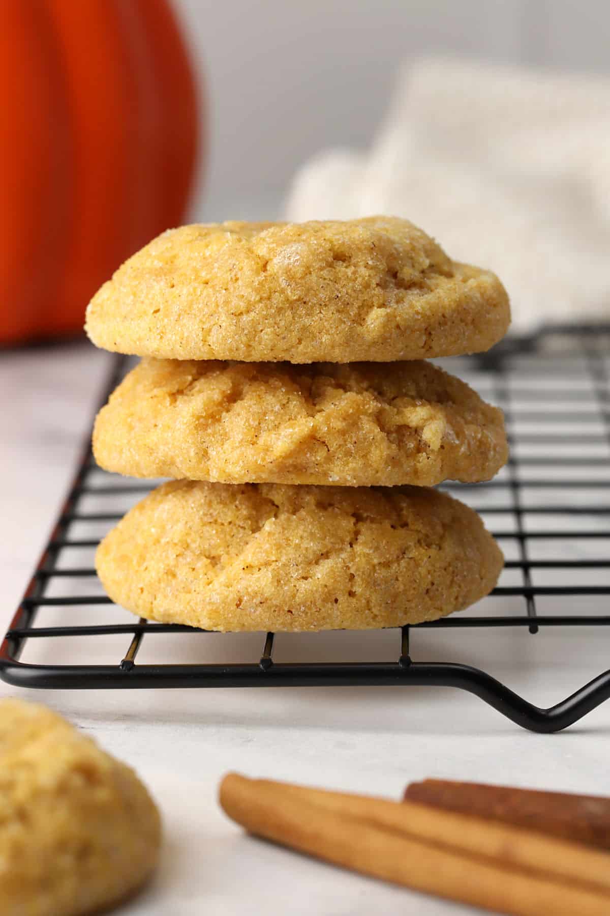 Three pumpkin sugar cookies stacked on a cooling rack.
