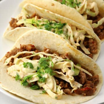 Closeup of Thai pork tacos topped with slaw on a plate.