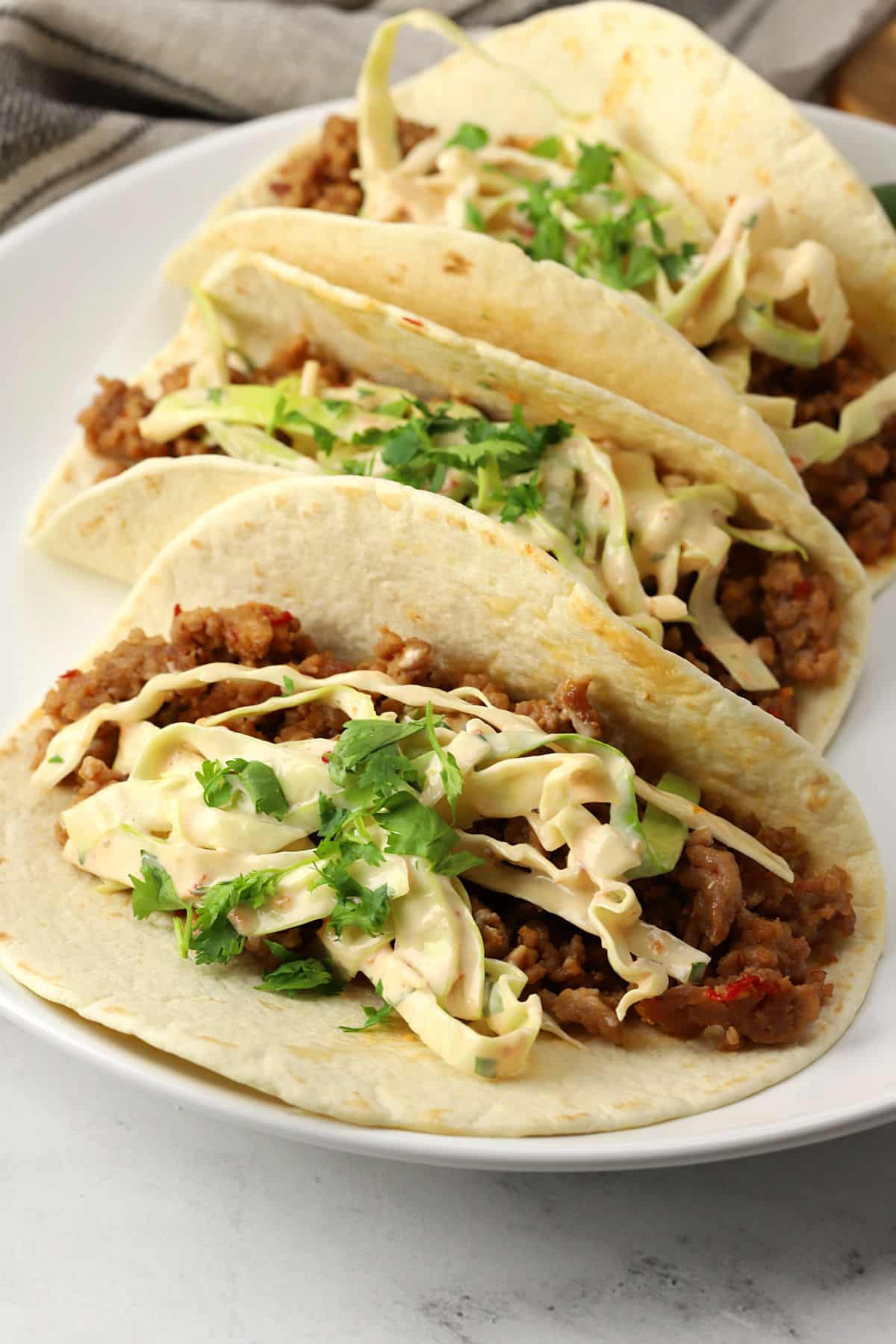 Closeup of Thai pork tacos topped with slaw on a plate.