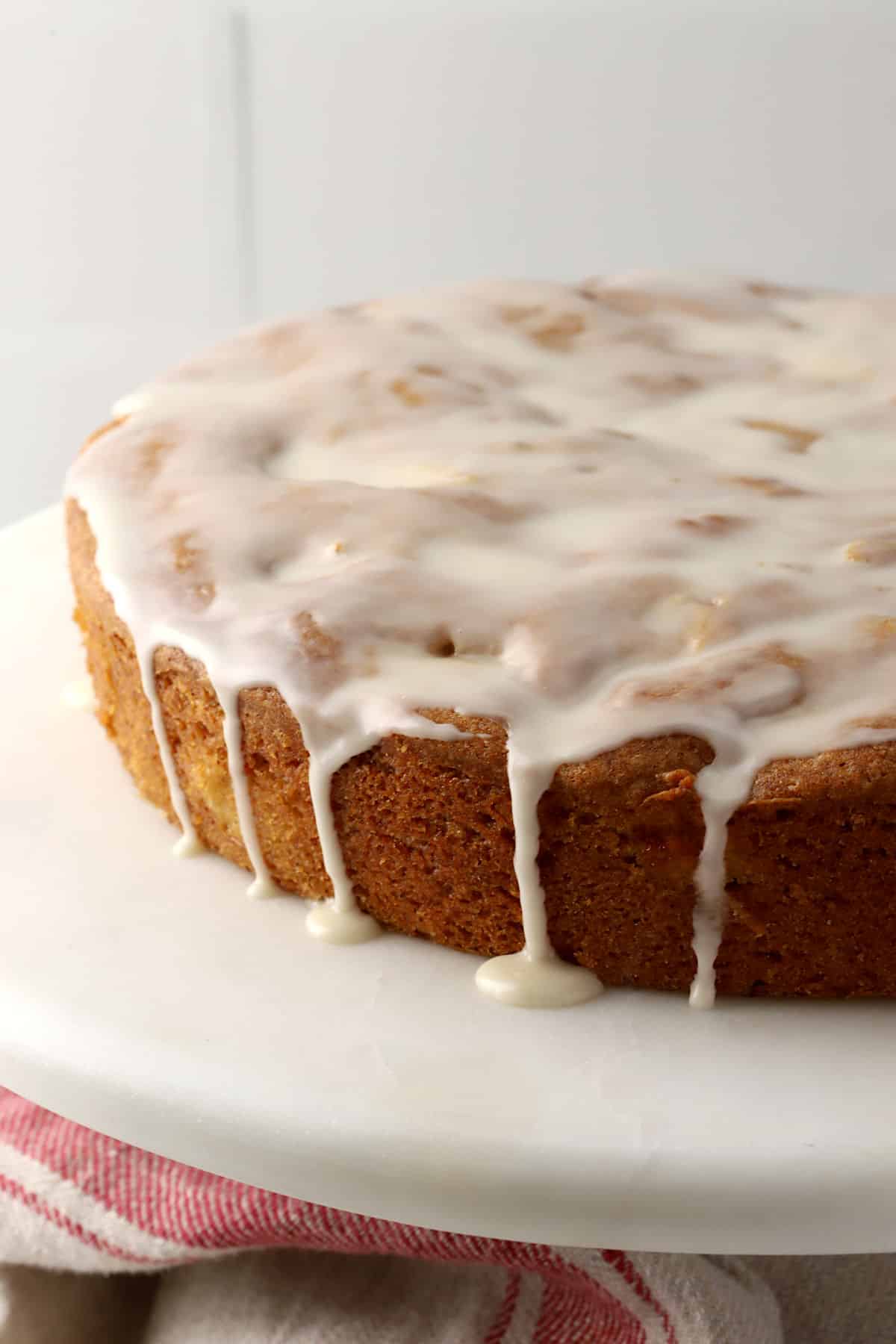 An apple fritter cake on a cake plate with icing dripping down the sides.