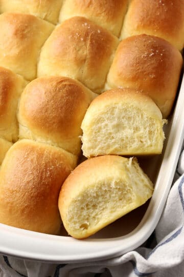 Two dinner rolls displayed with others in a baking pan.