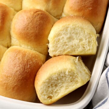 Two dinner rolls displayed with others in a baking pan.
