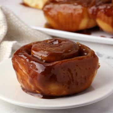 A caramel roll on a plate with more in the background.