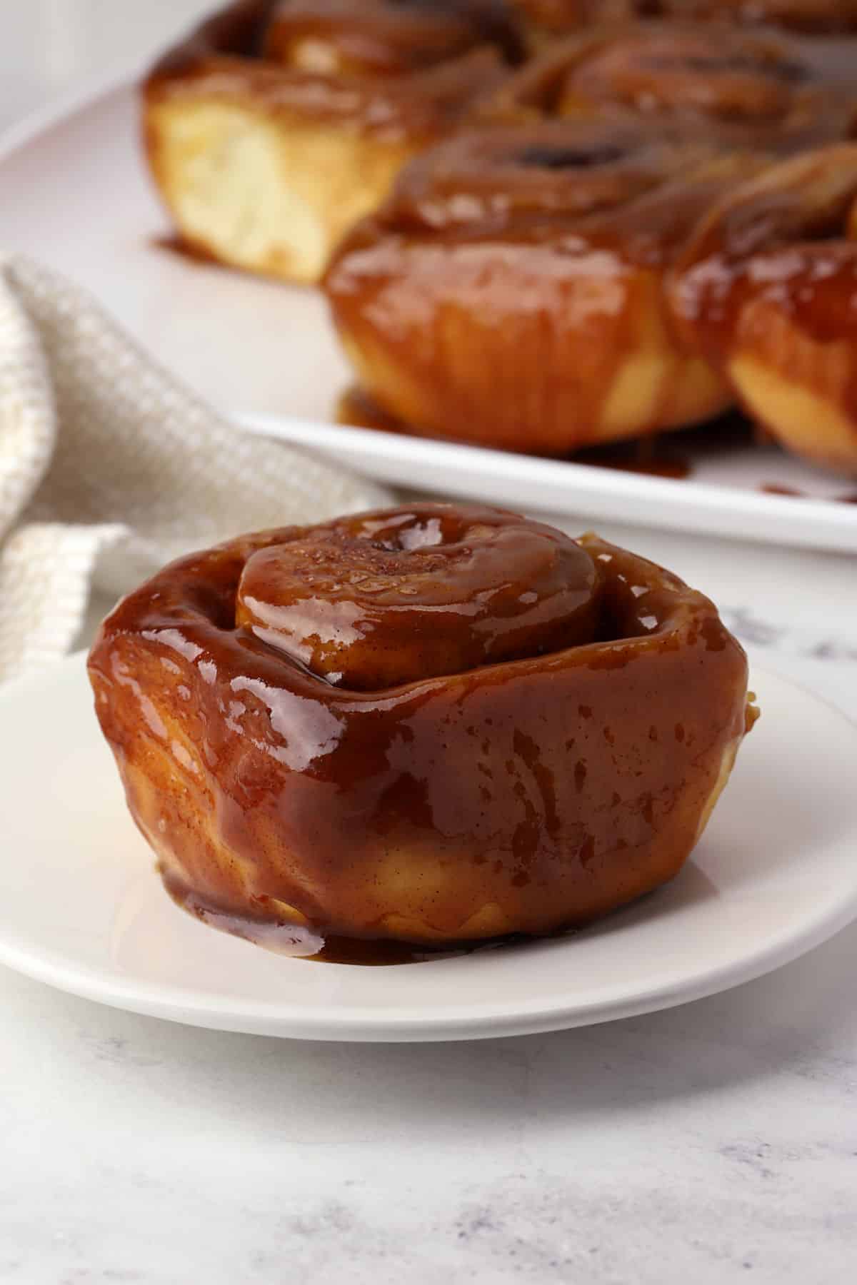 A caramel roll on a plate with more in the background.