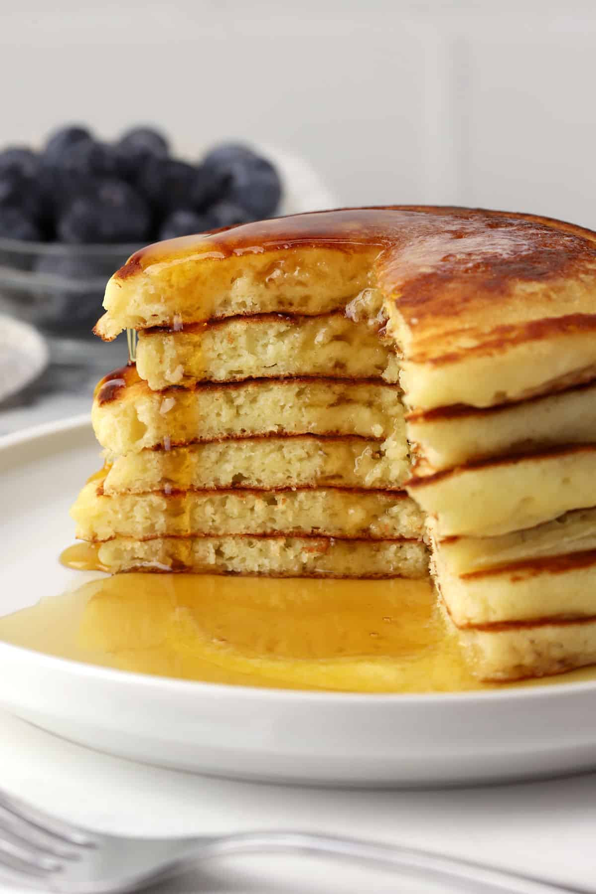 A stack of pancakes drenched in syrup with a wedge cut out of it.
