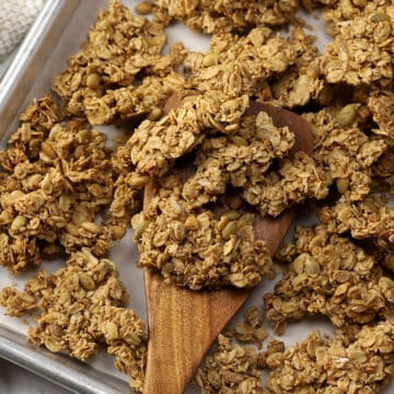 A wooden spatula scooping granola off of a sheet pan.