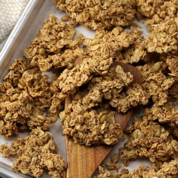 A wooden spatula scooping granola off of a sheet pan.