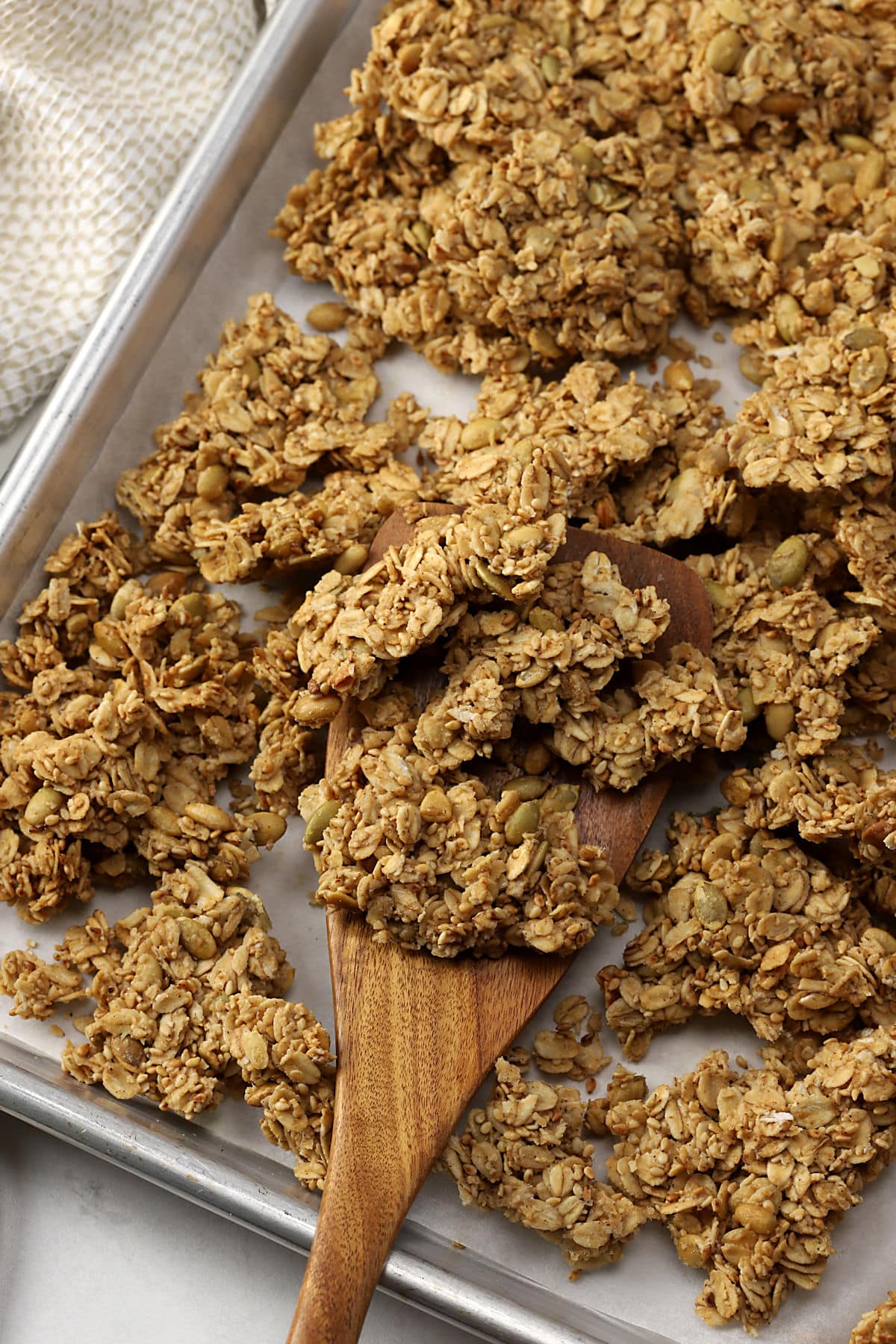 A wooden spatula scooping granola off of a sheet pan.