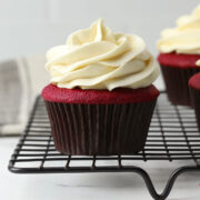 A frosted red velvet cupcake on a cooling rack.