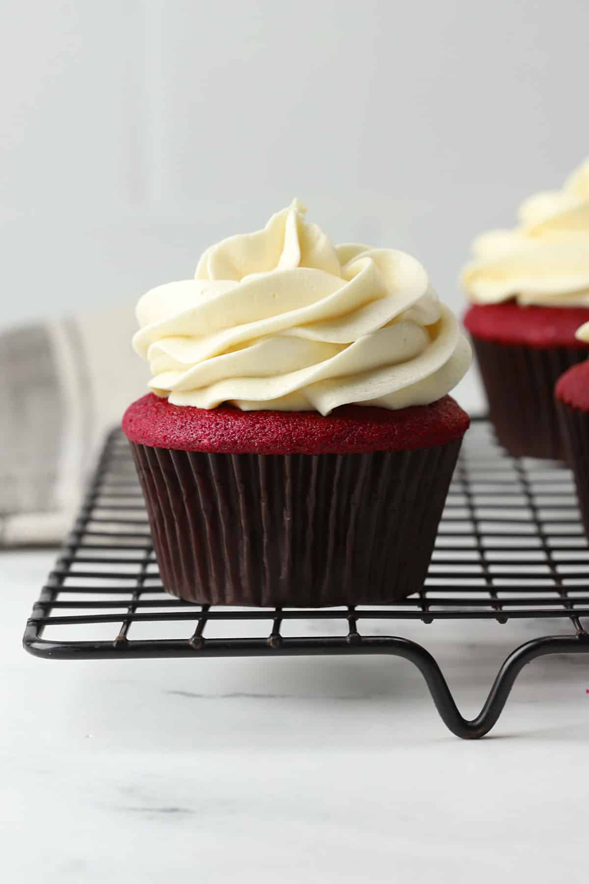 A frosted red velvet cupcake on a cooling rack.