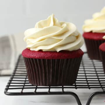 A frosted red velvet cupcake on a cooling rack.