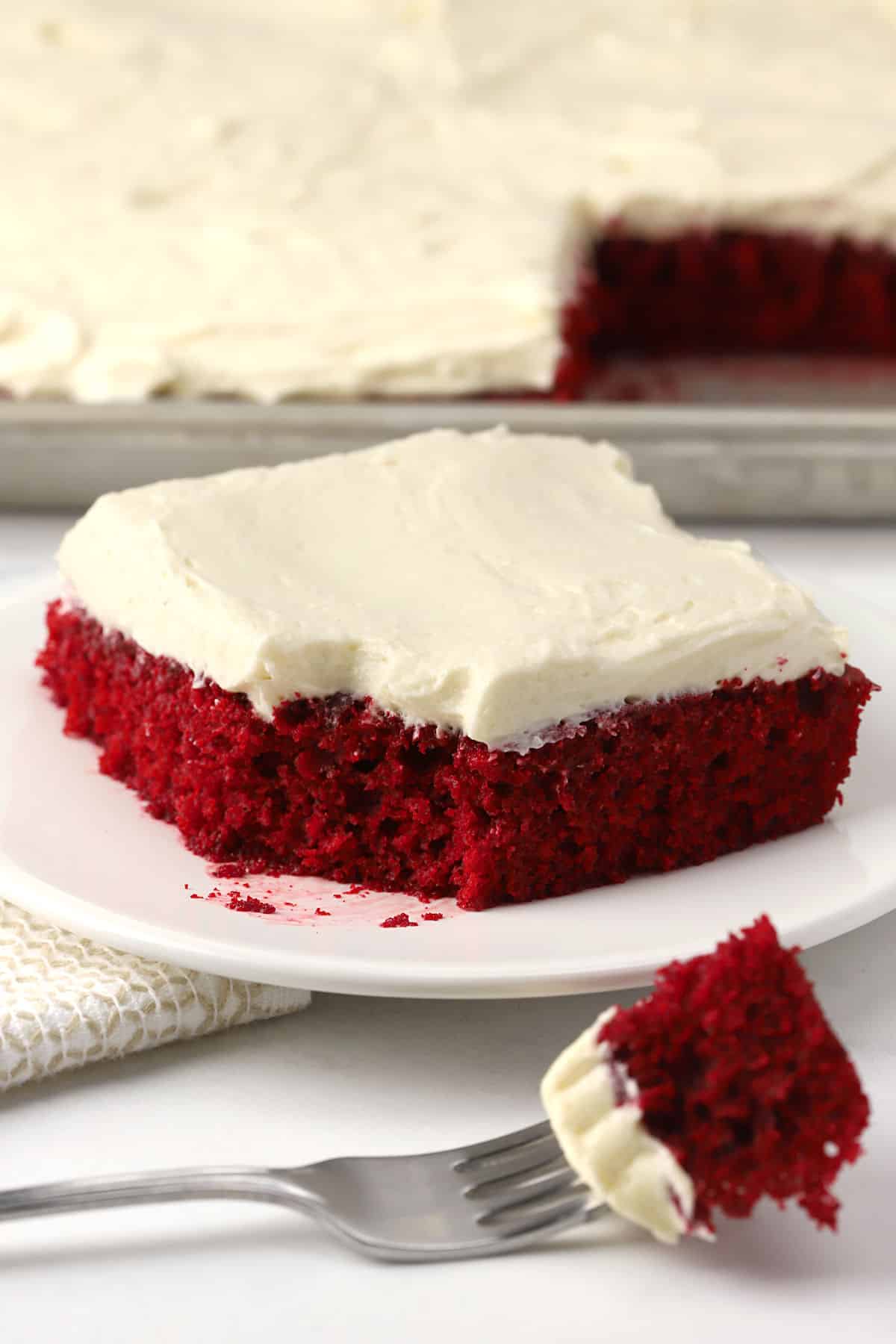A slice of red velvet cake with a forkful cut out and displayed.