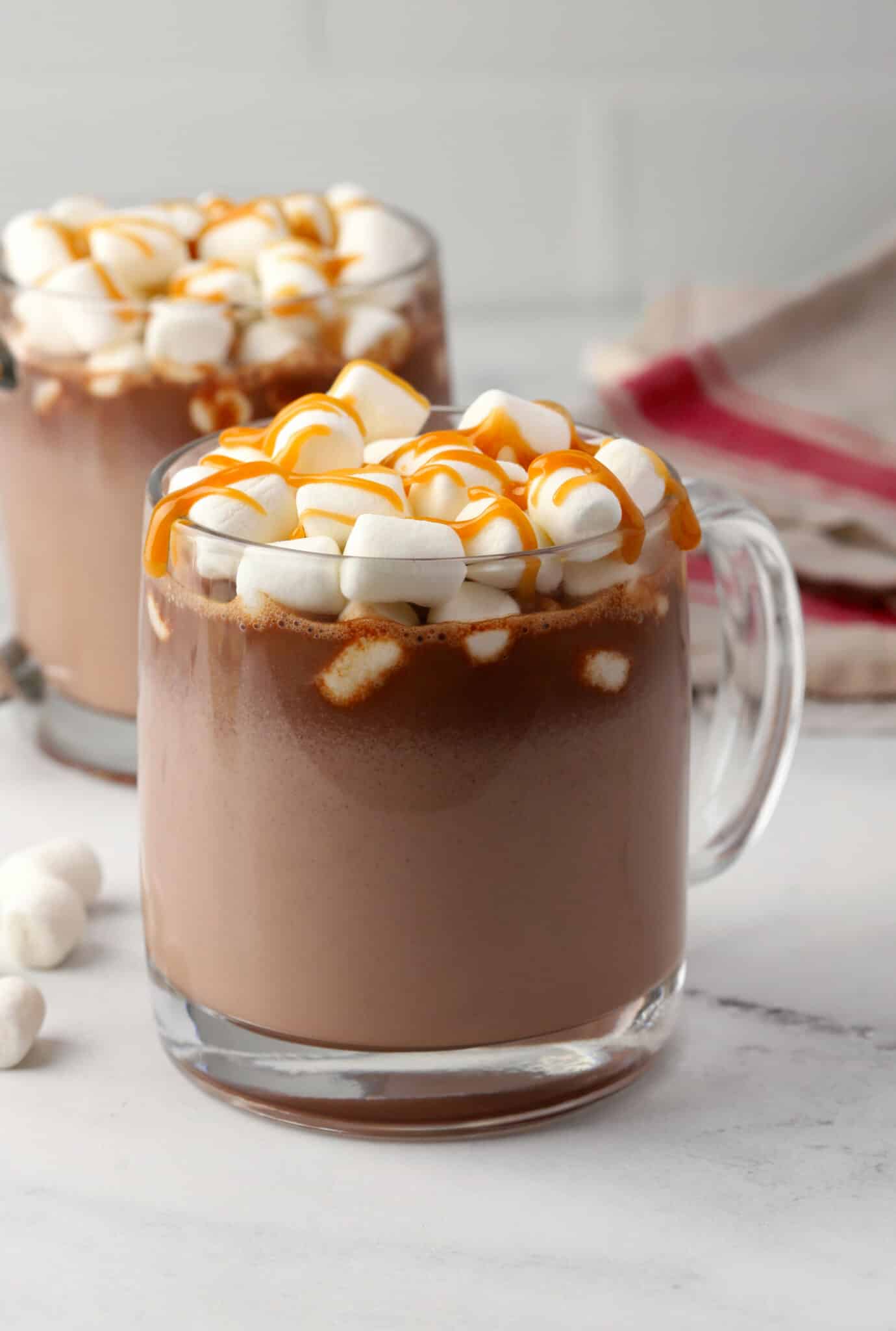 Glass mug of hot chocolate with salted caramel sauce on top.