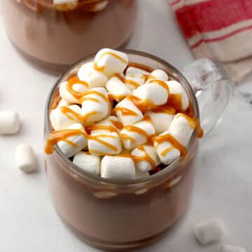 Mug of hot chocolate with marshmallows and caramel sauce on top.