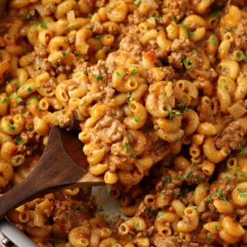 A wooden serving spoon scooping hamburger helper out of a saute pan.