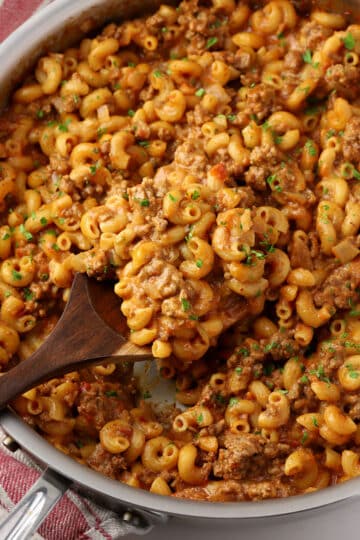 A wooden serving spoon scooping hamburger helper out of a saute pan.
