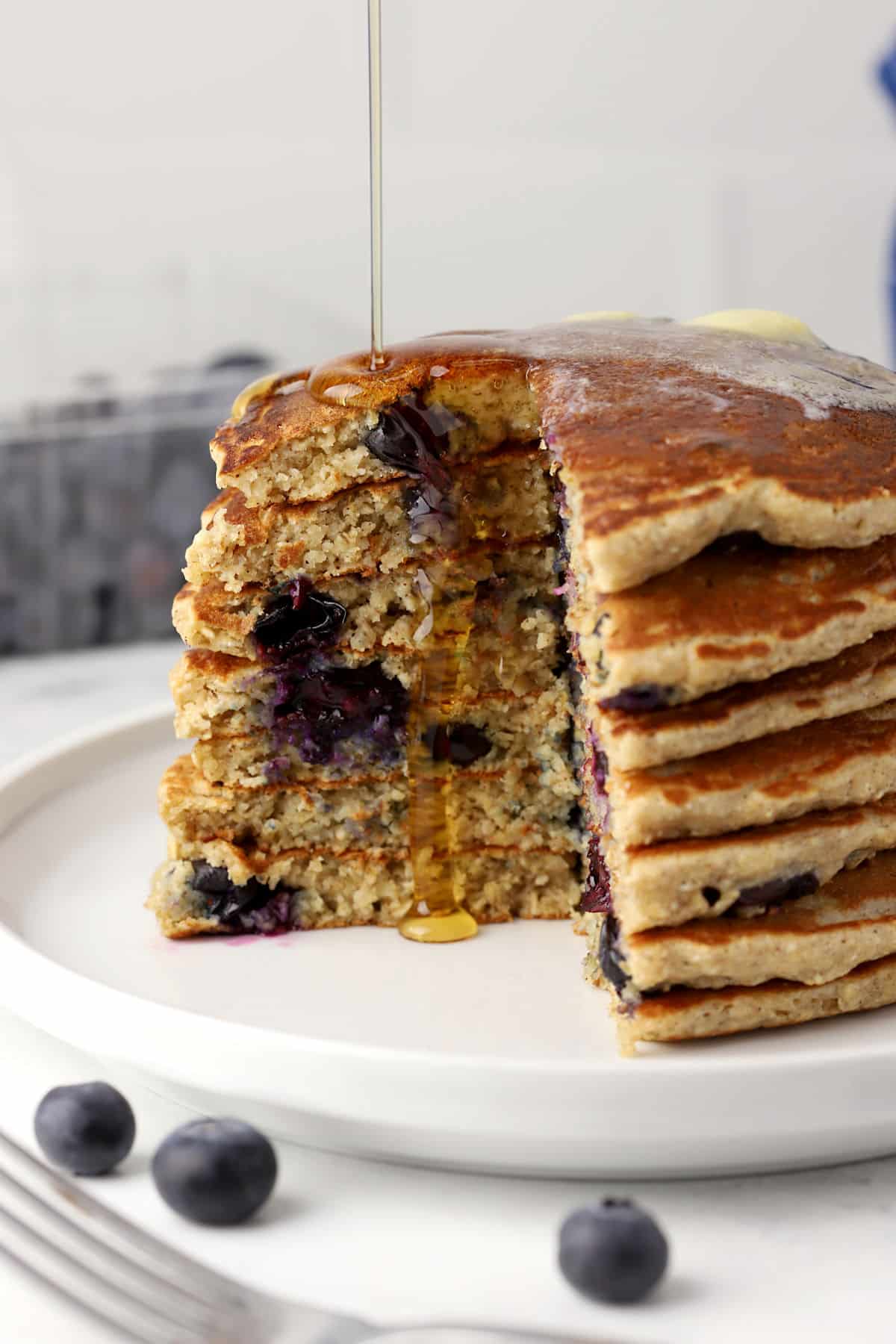 A stack of blueberry pancakes sliced with maple syrup.