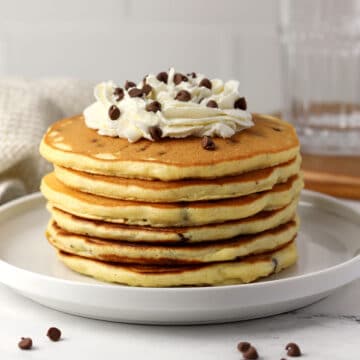 A stack of chocolate chip pancakes topped with whipped cream.