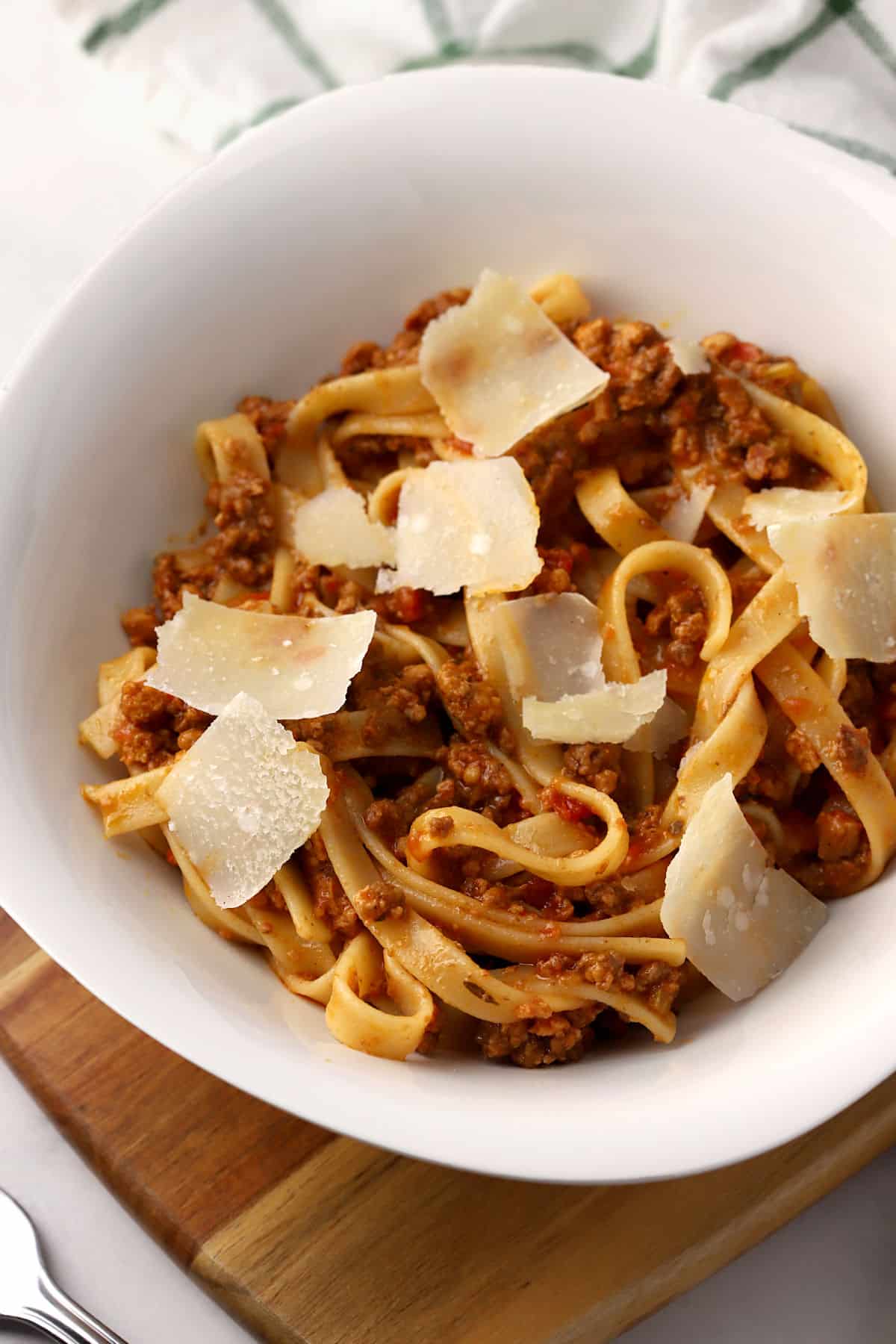 A plate of fettuccine bolognese with shaved parmesan on top.