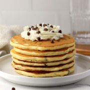 A stack of chocolate chip pancakes topped with whipped cream.
