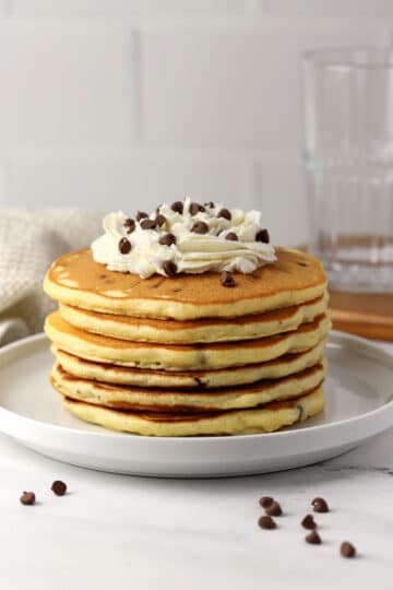 A stack of chocolate chip pancakes topped with whipped cream.
