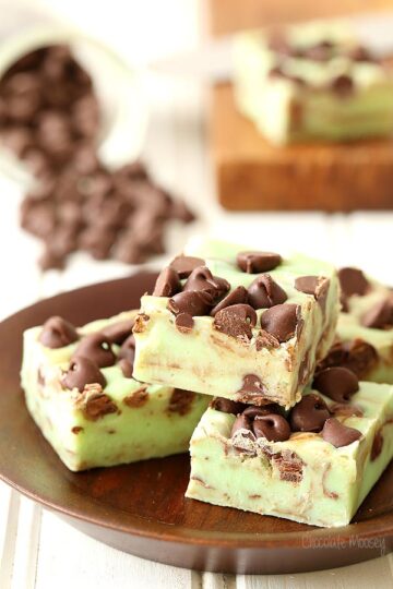 Squares of mint chocolate chip fudge stacked on a wooden plate.