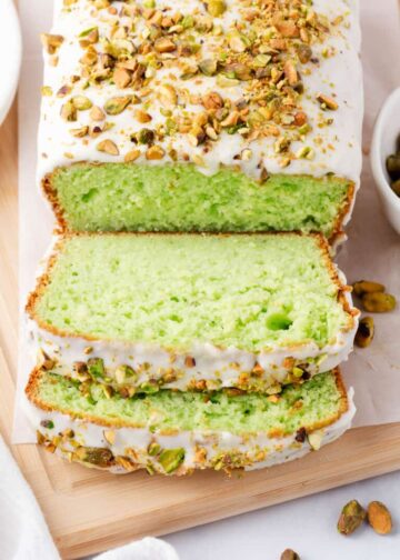 A loaf of pistachio bread iced and sliced on a cutting board.