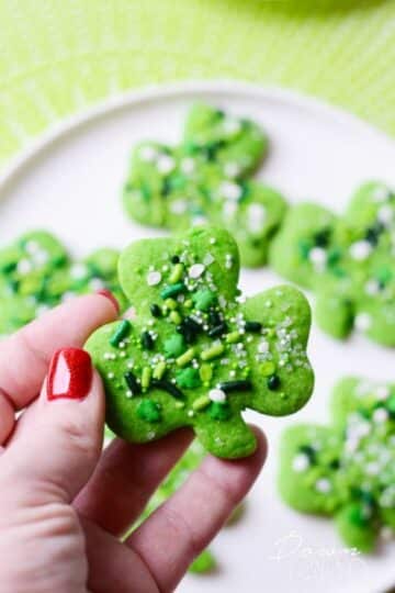 A hand holding a shamrock shaped cookie.