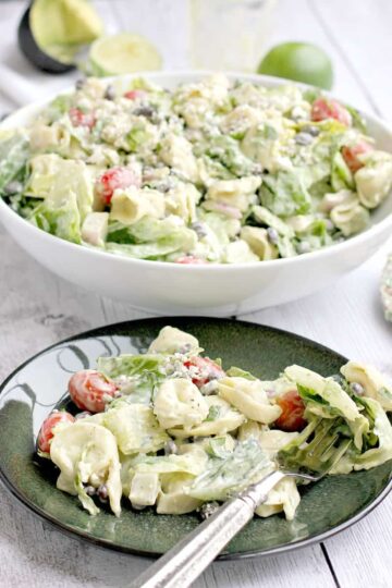 A plate and serving bowl with avocado and tortellini in a creaming dressing.