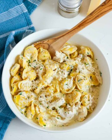 A bowl of tortellini in cream sauce with a wooden serving spoon.