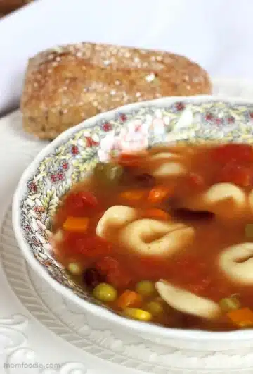 A bowl of soup with tortellini and vegetables.