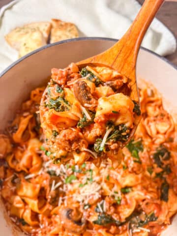 A wooden spoon full of sausage and tortellini pieces.