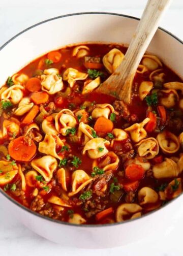 A pot of soup with tortellini, vegetables, and sausage.