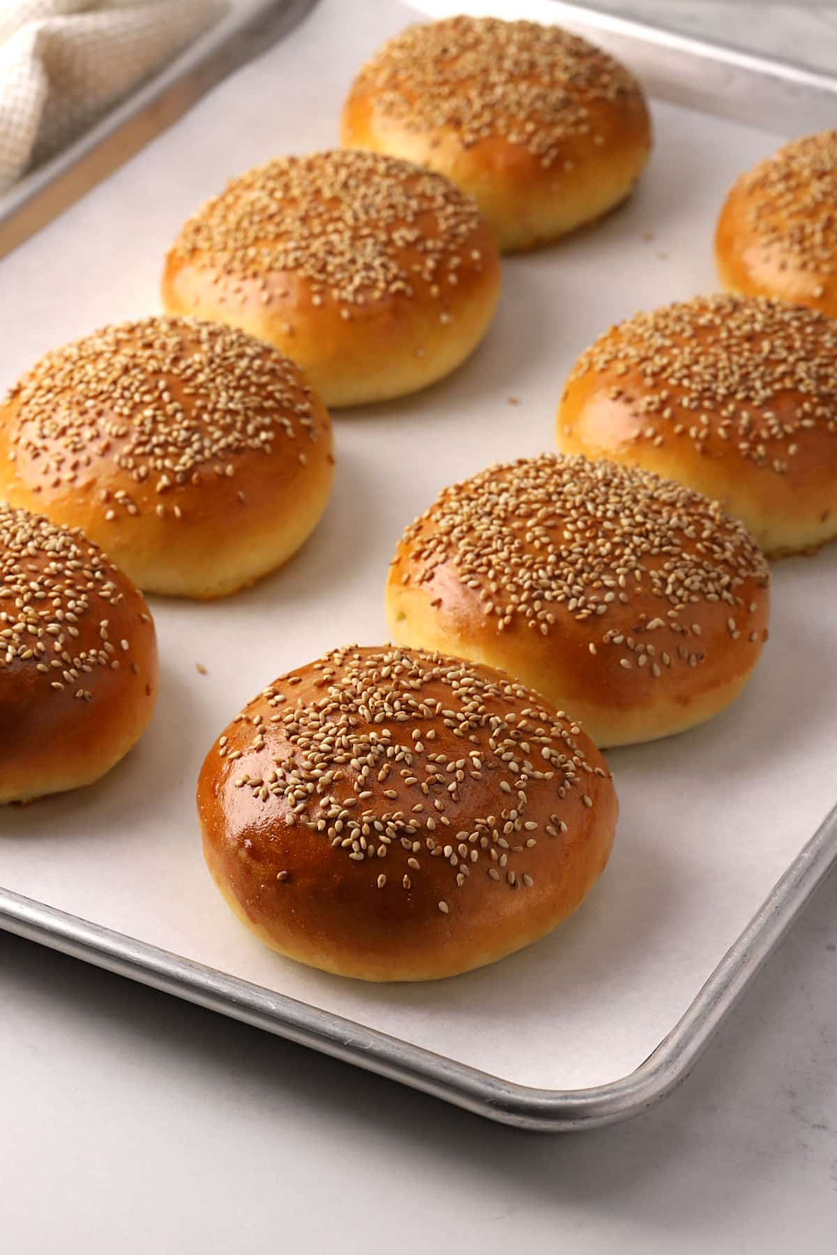 A baking sheet with hamburger buns on parchment.