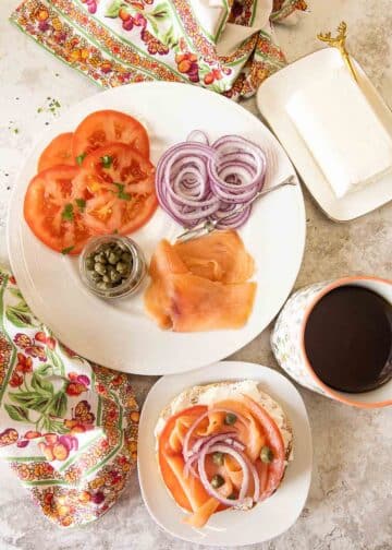 A spread featuring tomatoes, red onions, capers, salmon, cream cheese, and a bagel.