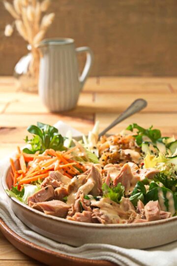 A bowl of salad heavy with toppings and dressing.