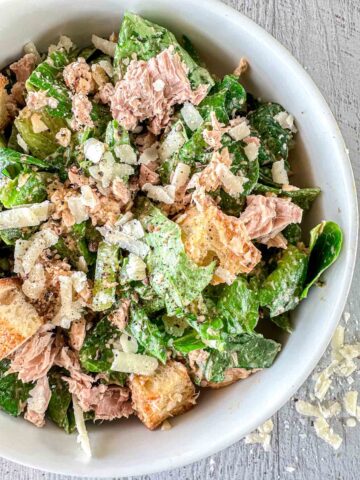 A bowl of caesar salad with tuna and croutons.