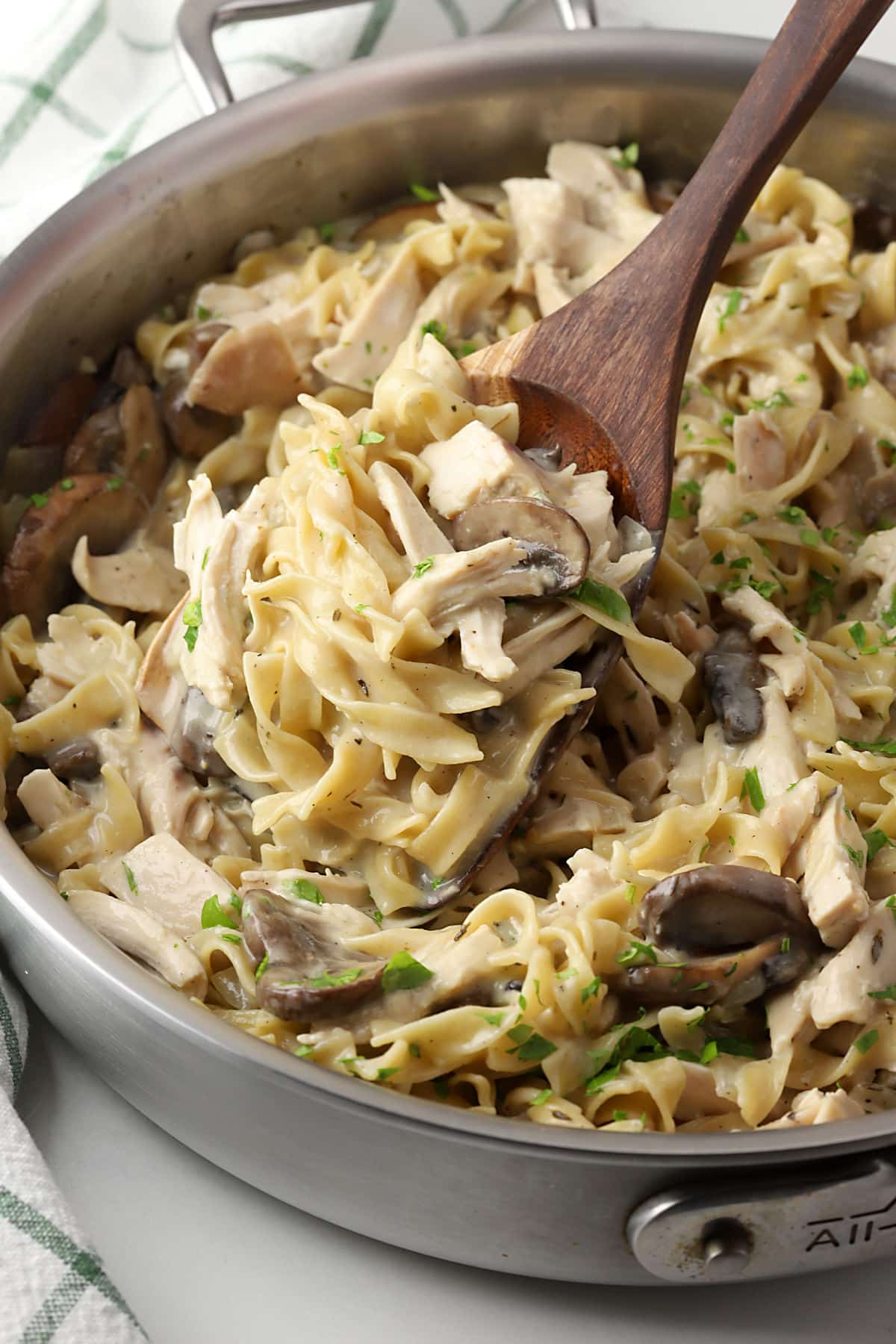 Spatula scooping chicken and noodles from a pan.