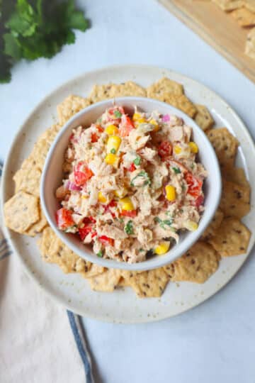 A bowl of tuna and corn salad with seasoned crackers.