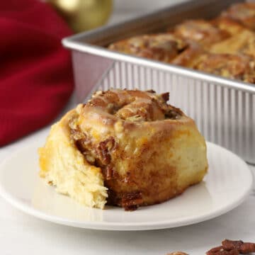 A cinnamon roll on a plate with a pan in the background.