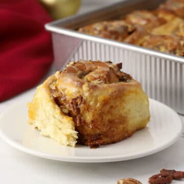 A cinnamon roll on a plate with a pan in the background.